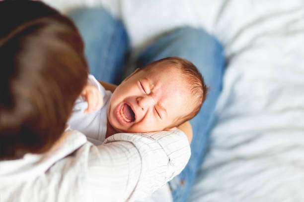 Crying baby held by parent, needs baby sleep sack comfort.