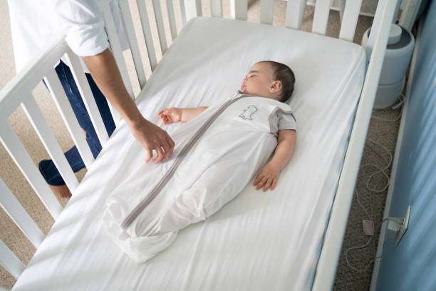 Baby sleeping peacefully in crib wearing a white baby sleep sack.