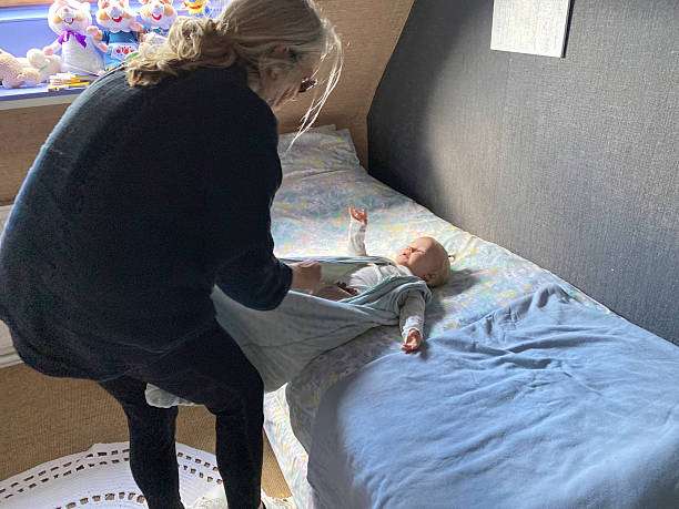 Parent gently placing a baby into a light blue baby sleep sack on the bed.