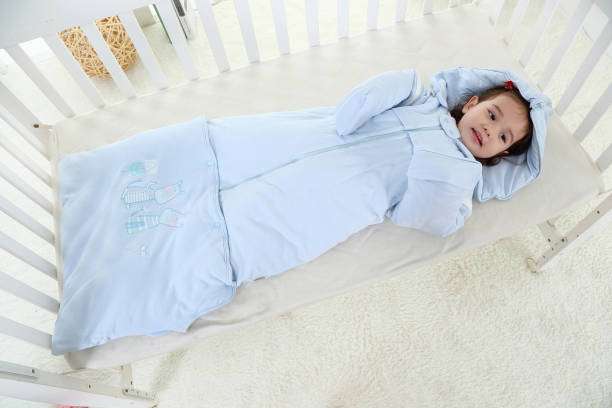 The baby is lying in bed wearing a Baby Sleep Sack.