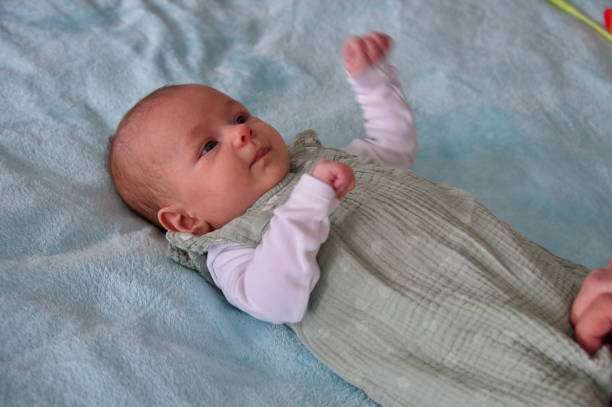 The baby is lying in bed wearing a Baby Sleep Sack.