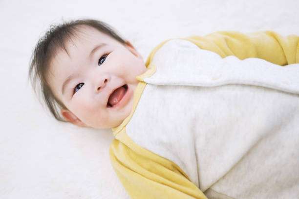 Happy baby lying on back, ready for peaceful sleep in a comfy Baby Sleep Sack.
