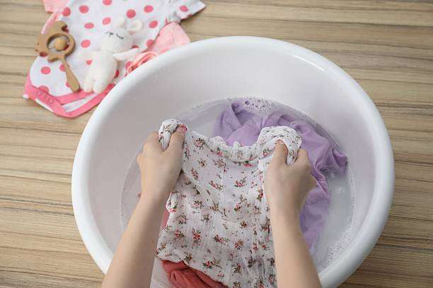 Washing delicate baby clothes by hand in a basin, ready for a clean baby sleep sack.